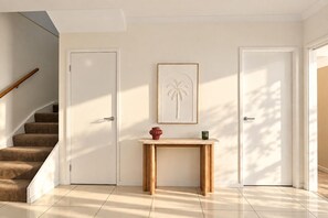 Un intérieur moderne avec un escalier, deux portes, un tableau encadré et une petite table en bois.
