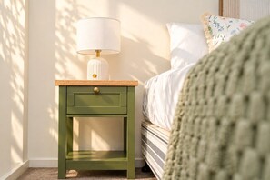 A green nightstand with a lamp and a drawer, positioned next to a bed with white bedding and a floral pillow. - Coastal-Style 3BR Townhouse - Mountain Creek (Mountain Creek)