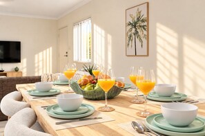 A breakfast setting with a wooden table, bowls, glasses of orange juice, and a fruit basket. - Coastal-Style 3BR Townhouse - Mountain Creek (Mountain Creek)