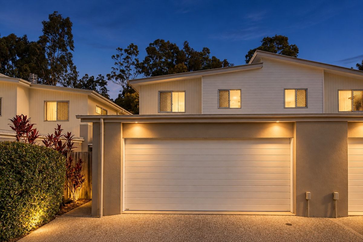 A modern two-story house with a garage, a well-maintained lawn, and a clear sky.