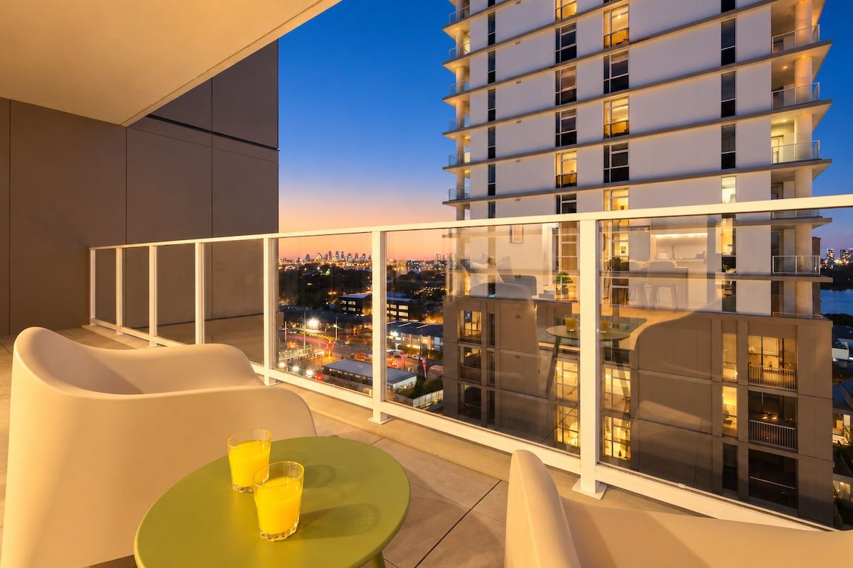 A balcony with a table and chairs, overlooking a cityscape at dusk.