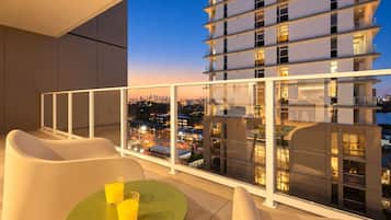A balcony with a table and chairs, overlooking a cityscape at dusk.
