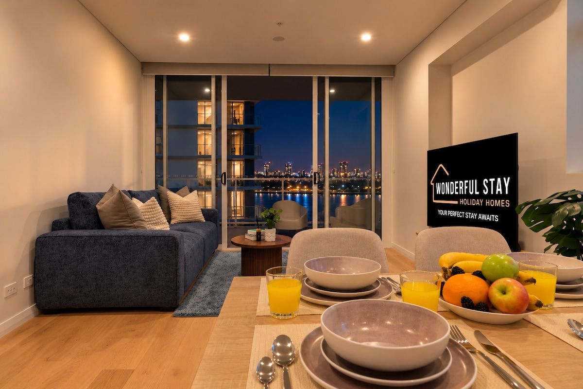 A modern living room with a sofa, dining table set with plates, bowls, and fruit, and a city view through large windows.