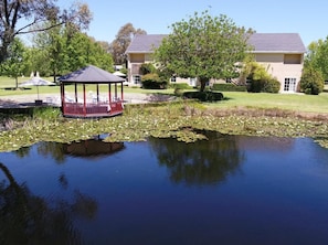 A gazebo by a pond with a lawn and buildings in the background. - Peel Manor House (Karnup)