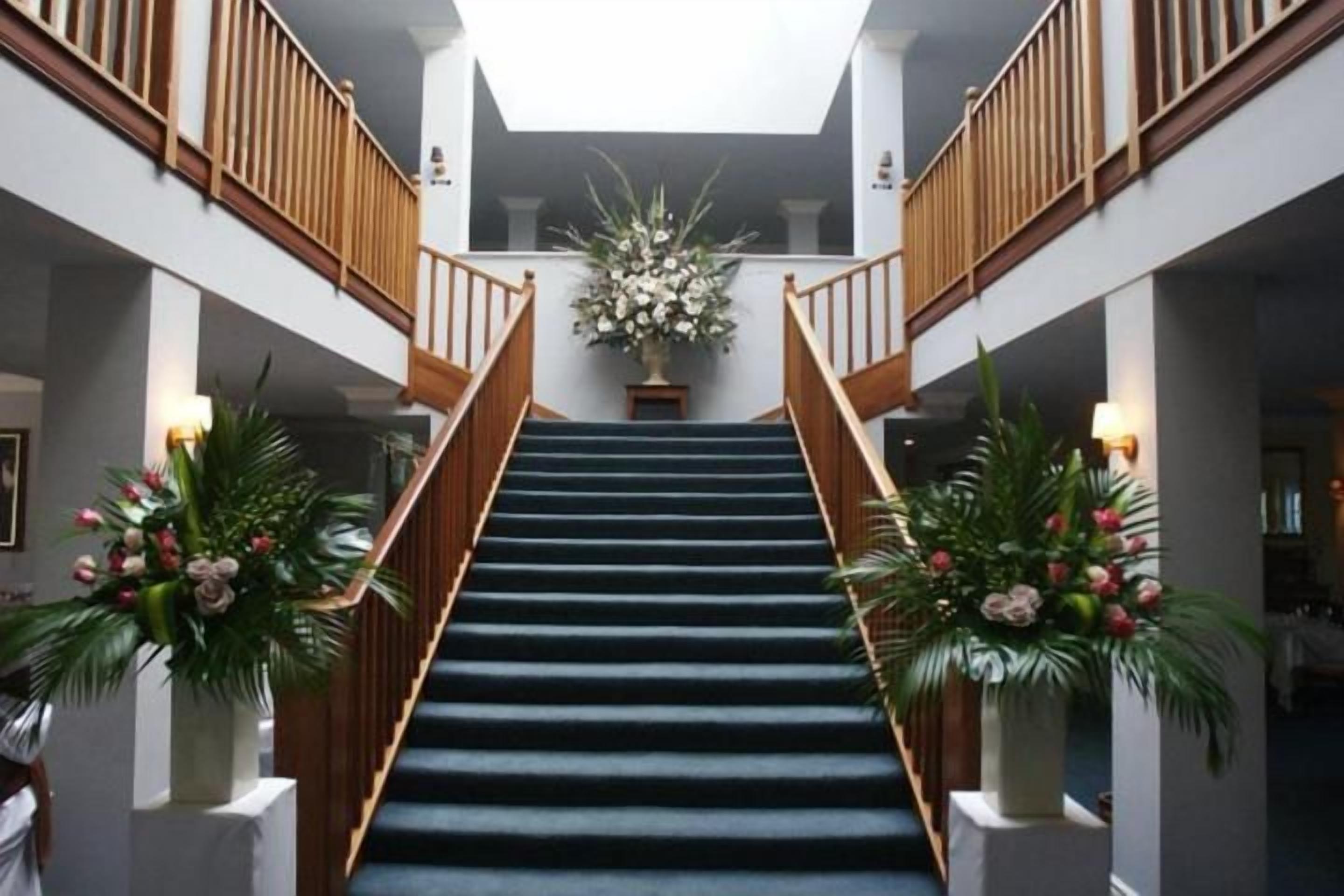 Una escalera con barandillas de madera, flanqueada por macetas con plantas, que conduce a un segundo piso.