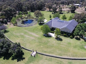 An aerial view of a large house with a well-maintained lawn, a pond, and a bridge leading to the property. - Peel Manor House (Karnup)