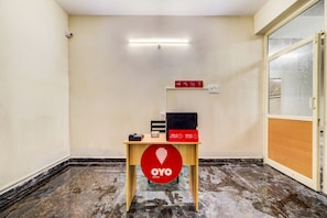 Habitació amb escriptori de fusta, un cartell vermell d'OYO, una impressora negra i una làmpada fixa a la paret.