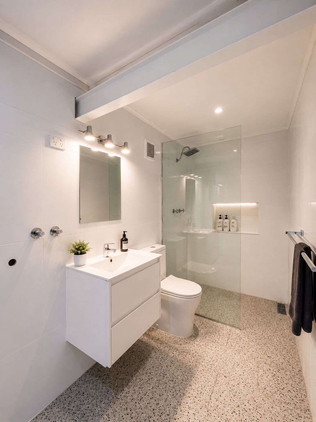A modern bathroom with a white vanity, a glass shower enclosure, and a toilet.