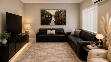 A modern living room with a flat-screen TV, two sofas, a coffee table, and a large painting on the wall.