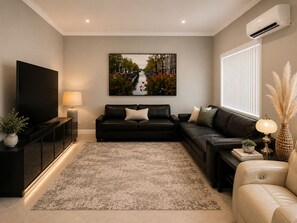 A modern living room with a flat-screen TV, two sofas, a coffee table, and a large painting on the wall. - Ocean-View Family Retreat w/ Games Room, Balcony & Backyard, Wollongong (Cringila)