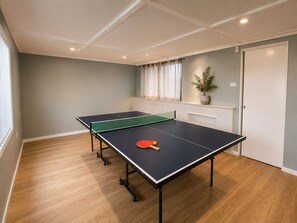 A room with a ping pong table, a potted plant, and a window with curtains. - Ocean-View Family Retreat w/ Games Room, Balcony & Backyard, Wollongong (Cringila)