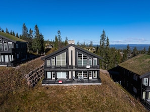 Une maison moderne à deux étages, dotée d’un toit à forte pente, de grandes fenêtres et d’un balcon.