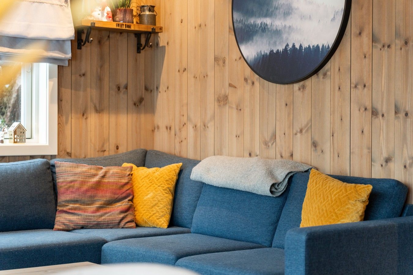 Ein Wohnzimmer mit einem blauen Sofa, einem Fenster mit Blick auf Bäume und einer Holzwand.