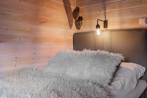 A room with a wooden wall, a bed with a fluffy white blanket, and a wall-mounted light fixture. - FA301 Top-Floor flat with Sauna, Three Balconies (Trysil)