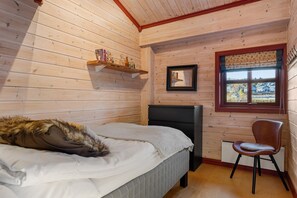 A wooden cabin bedroom with a bed, a chair, a shelf with books and bottles, a window with a view, and a framed picture on the wall. - FA301 Top-Floor flat with Sauna, Three Balconies (Trysil)