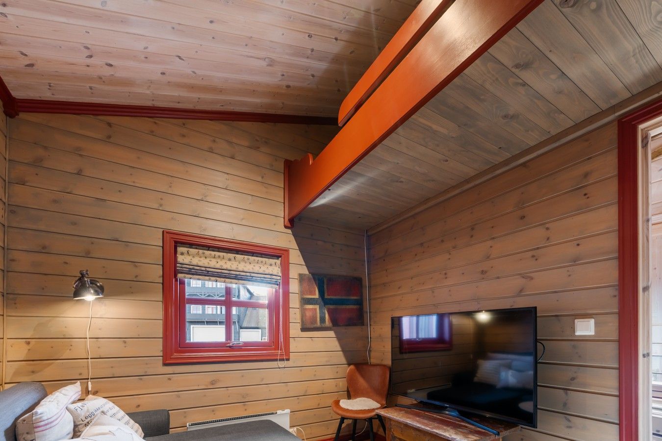 L’intérieur d’un chalet en bois, avec une télévision, une fenêtre dotée d’un cadre rouge et une lampe.
