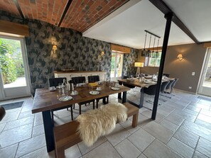 A dining area with a large wooden table, benches, and chairs. There is a fireplace with a mantel, and the room has patterned wallpaper and a tiled floor. - Holiday Home 'Gîte Givonne' for 15 People near Bouillon (Givonne)