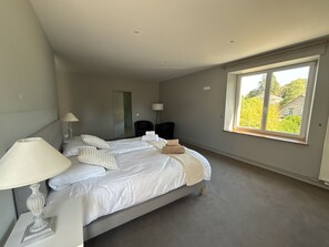 Ein Schlafzimmer mit einem Bett, Nachttischlampen, einem Fenster und Blick ins Grüne.