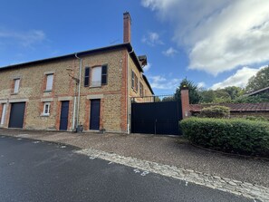 A two-story stone building with a black gate, a paved driveway, and a clear sky. - Holiday Home 'Gîte Givonne' for 15 People near Bouillon (Givonne)