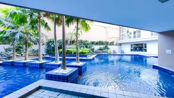 An indoor swimming pool with tiled flooring and palm trees.