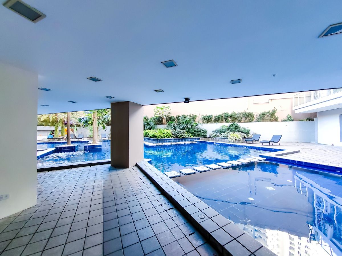 A swimming pool with a tiled deck and lounge chairs, surrounded by greenery.