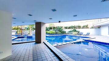 A swimming pool with a tiled deck and lounge chairs, surrounded by greenery.