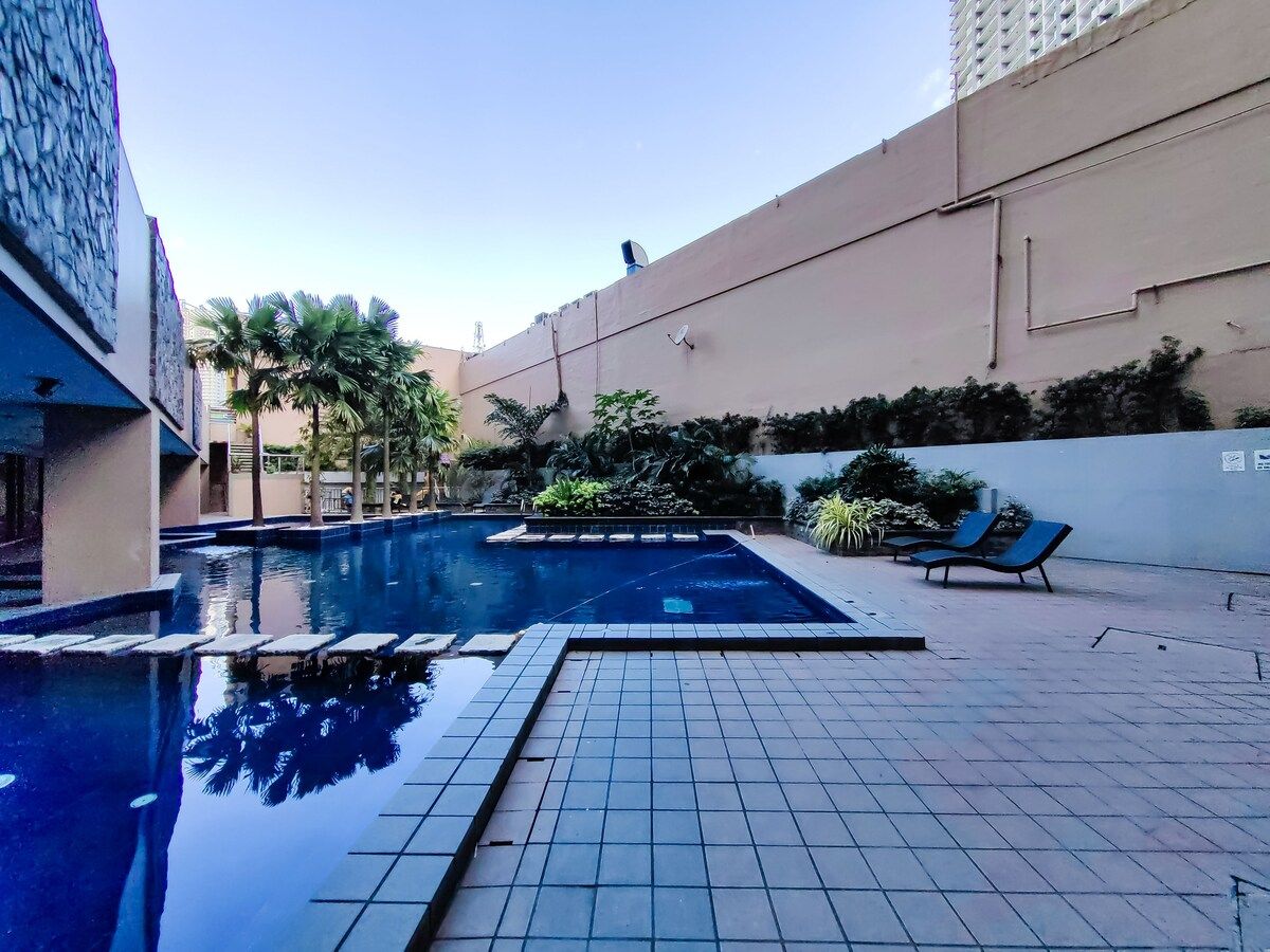A swimming pool with a tiled deck, lounge chairs, and a view of a building in the background.