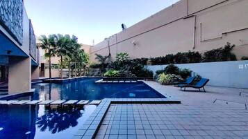 A swimming pool with a tiled deck, lounge chairs, and a view of a building in the background.