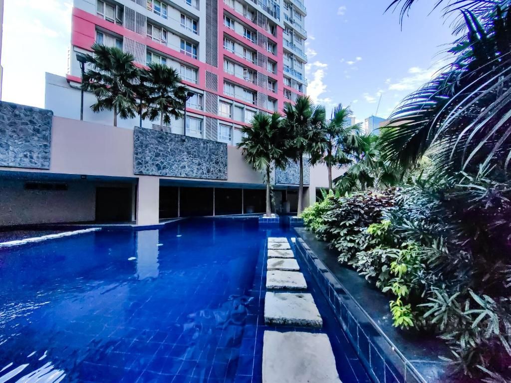 A swimming pool with stone steps leading into it, surrounded by tropical plants and a multi-story building with balconies.