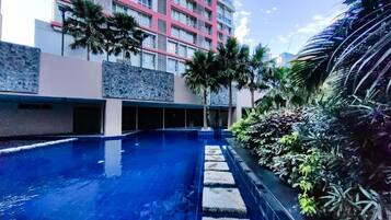 A swimming pool with stone steps leading into it, surrounded by tropical plants and a multi-story building with balconies.