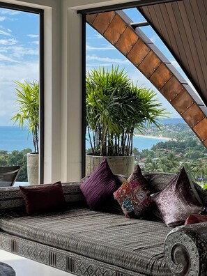 Ein Zimmer mit Meerblick, eine Couch mit gemusterten Kissen und Topfpflanzen.