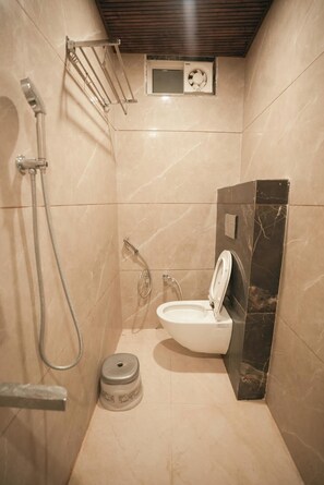 A compact bathroom with a toilet, a shower, and a small shelf with a fan. - Nandani Palace (Ayodhya)