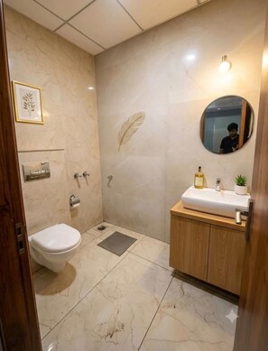 A bathroom with a toilet, sink, mirror, and a decorative leaf on the wall. - Nandani Palace (Ayodhya)