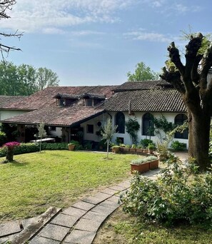 A two-story house with a tiled roof, a well-maintained lawn, and a stone pathway leading to the entrance. - Vrbo Property (Piemonte)