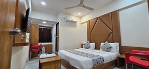 Habitación de hotel con cama, escritorio, silla, equipo de aire acondicionado y ventilador de techo.