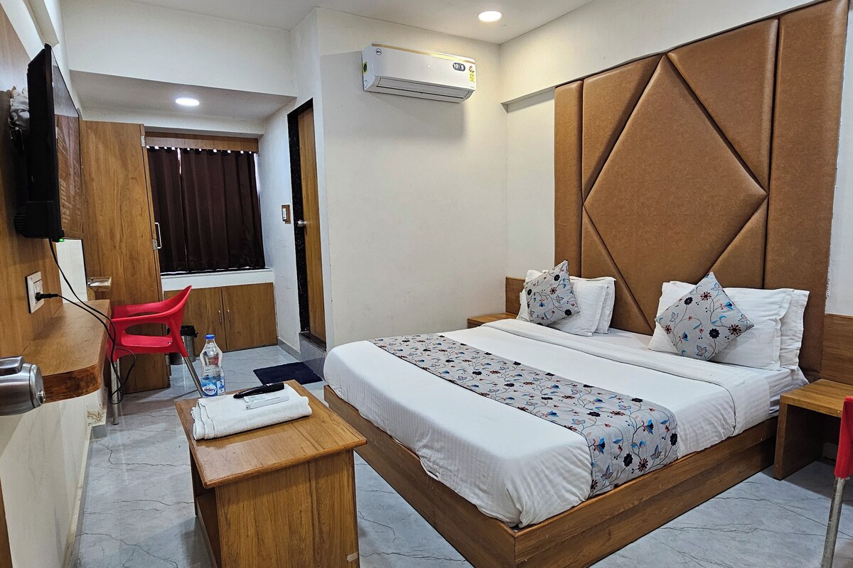 Habitación de hotel con cama, escritorio, silla, televisor y aire acondicionado.