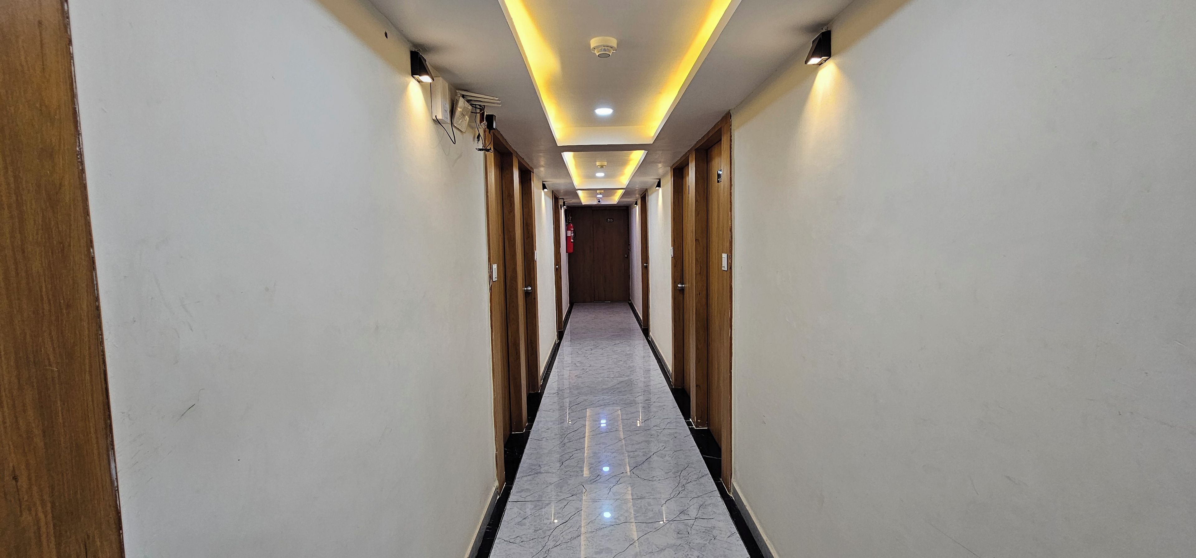 Pasillo de hotel con puertas de madera, suelo de mármol e iluminación empotrada.