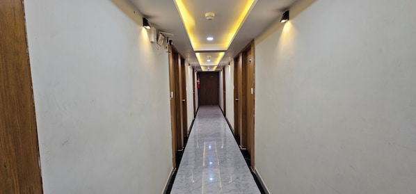A hotel corridor with wooden doors, a marble floor, and recessed lighting.