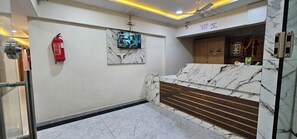 Un vestíbulo de hotel con mostrador de recepción de mármol, un extintor y una cámara de seguridad.