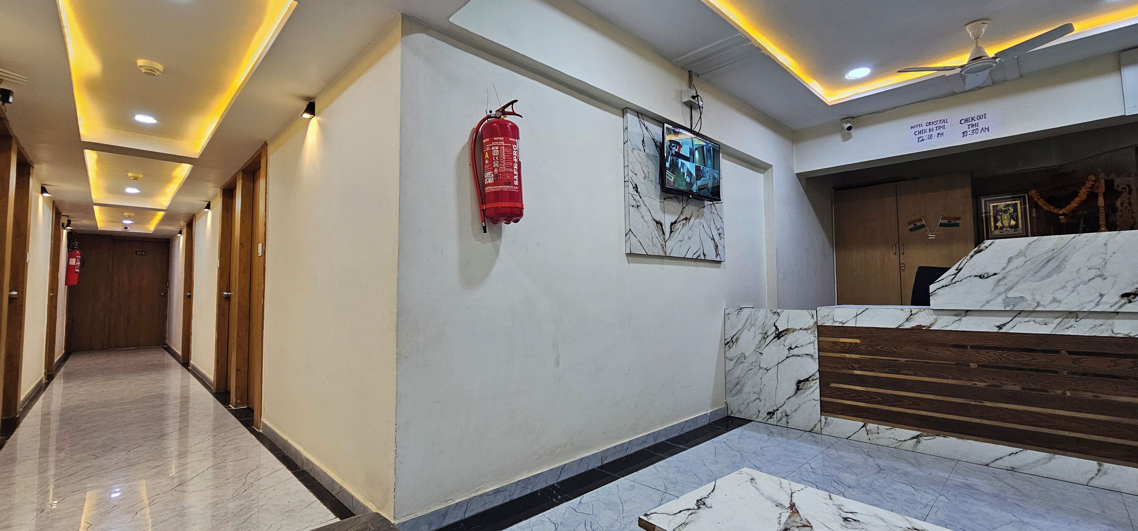 A hotel lobby with a marble reception desk, a fire extinguisher, a security camera, and a ceiling fan.
