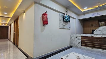 A hotel lobby with a marble reception desk, a fire extinguisher, a security camera, and a ceiling fan.
