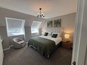 Een slaapkamer met een bed, een stoel, een nachtkastje, een lamp en een raam.