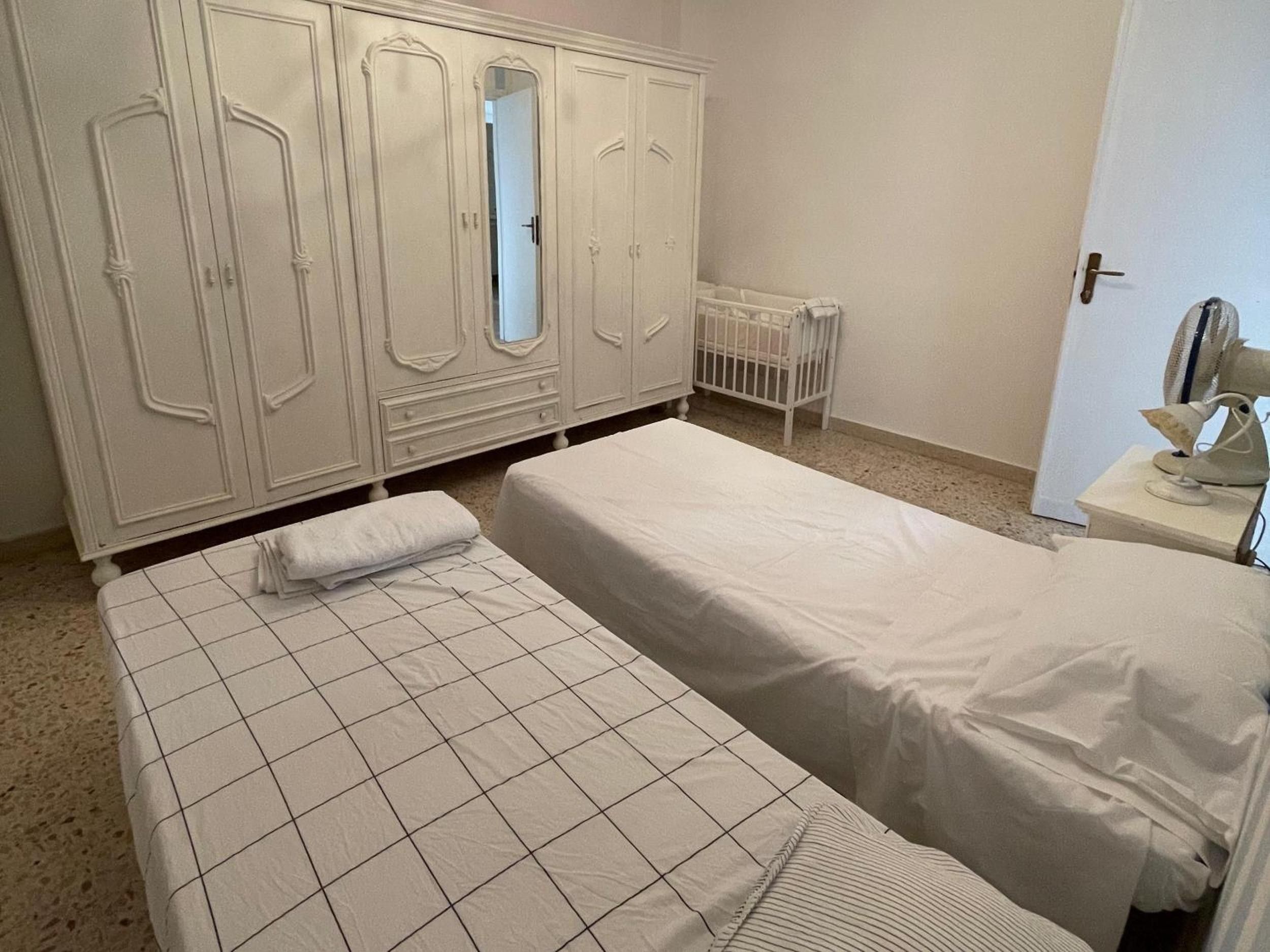 Una habitación con dos camas individuales, un armario blanco, un radiador y una mesita de noche con lámpara.