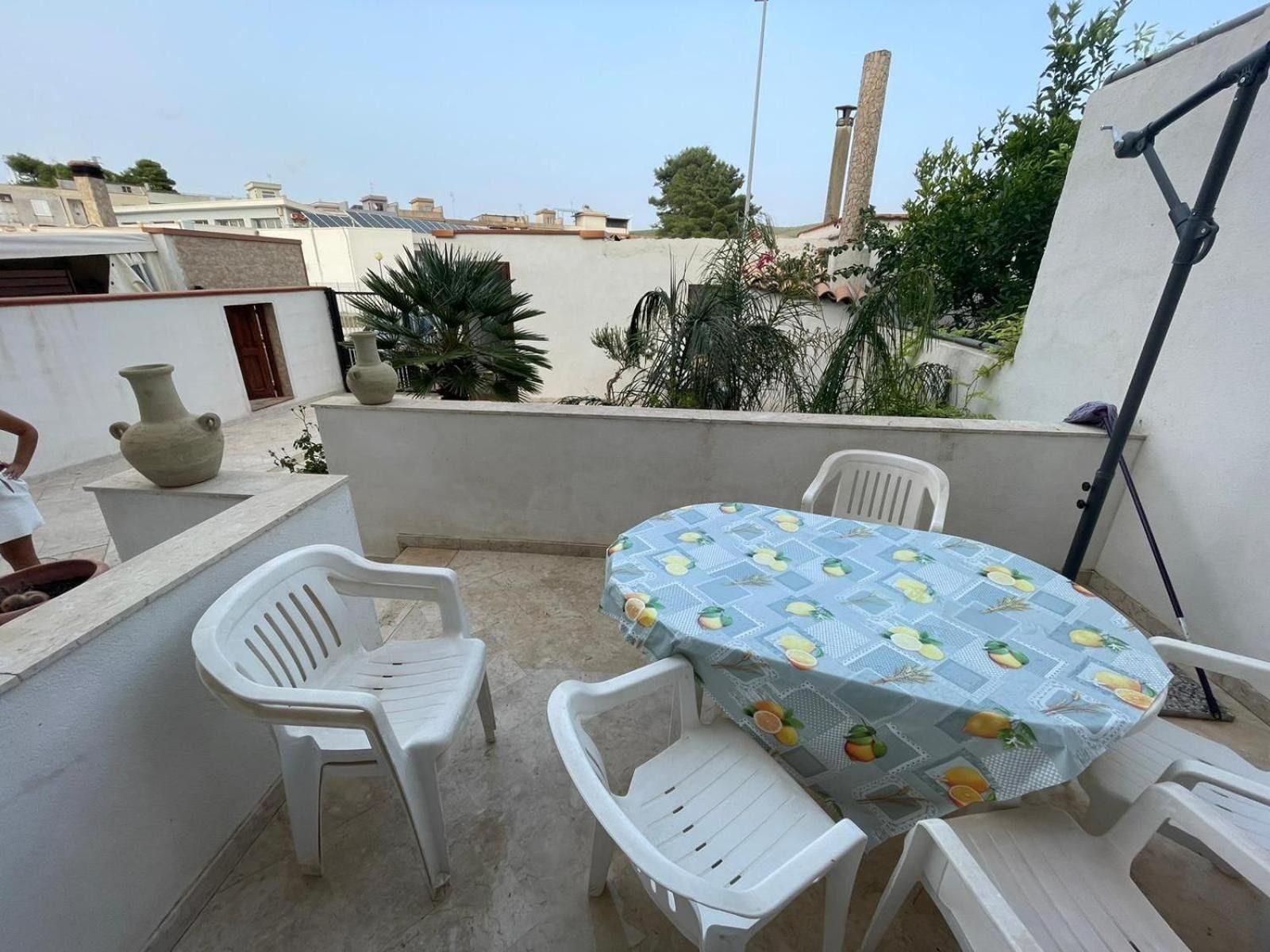 Terraza en la azotea con una mesa redonda y cuatro sillas, rodeada de plantas en macetas y vistas panorámicas de la ciudad.