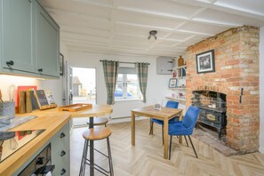 Een eetruimte met een haard van baksteen, een houten tafel en blauwe stoelen.