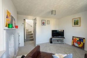 Ein Wohnzimmer mit Fernseher, einer Couch, einer Treppe und einem Bücherregal.