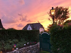 A traditional thatched-roof house with a stone wall and a green gate, set against a sunset sky. - Deichhof Apt. 23 (Dunsum)