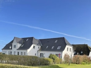 A two-story white building with a dark roof, surrounded by well-maintained hedges and a grassy lawn. - Deichhof Apt. 23 (Dunsum)