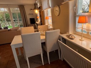 A dining area with a white table and chairs, a clock on the wall, and a window with curtains. - Deichhof Apt. 23 (Dunsum)