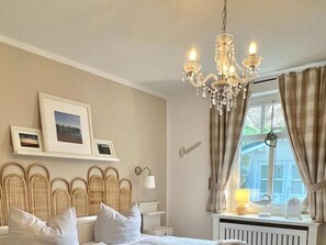 A bedroom with a bed, a chandelier, a window with curtains, and wall-mounted pictures. - Deichhof Apt. 23 (Dunsum)